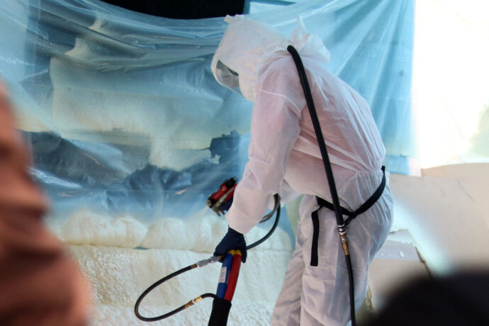 Technician demonstrates the PMC Xtreme air purge spray foam gun in action at Polyurethane Machinery Corporation booth, showcasing proportioner equipment during live spray foam application.